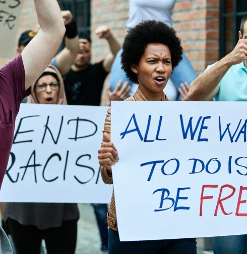 Large group of people  demonstrating against racism on the streets. Focus is on black woman carrying placard with freedom inscription.